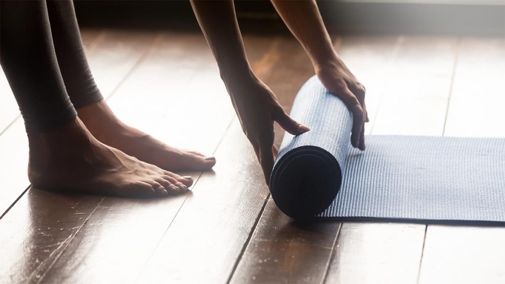 only hands and feet of a woman visible as she rolls up a yoga mat