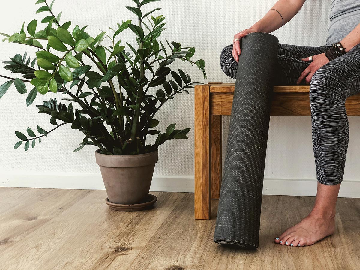 someone sitting indoors on a wooden bench with a rolled up yoga mat