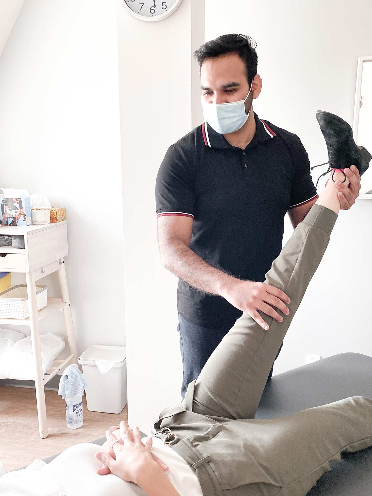 man wearing a surgical mask stretching the leg of a client who is lying down