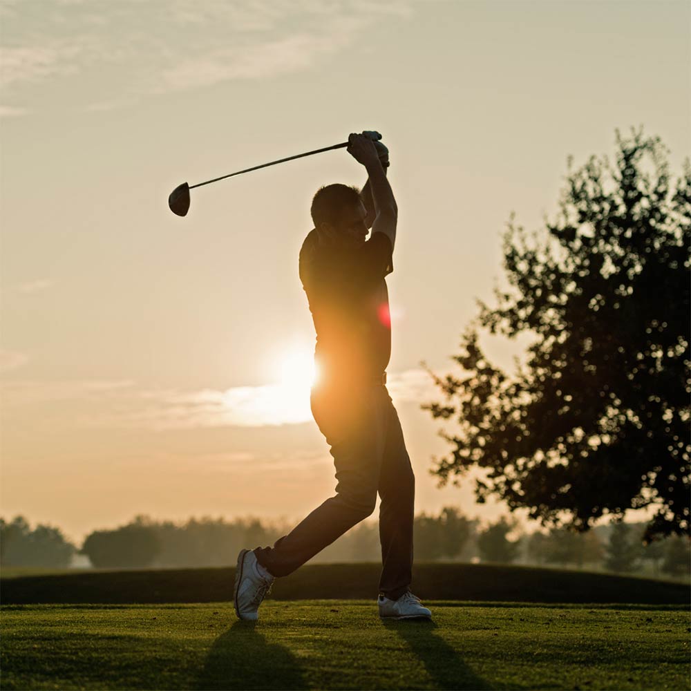 silhouette of a man swinginging a golf club with the setting sun behind him