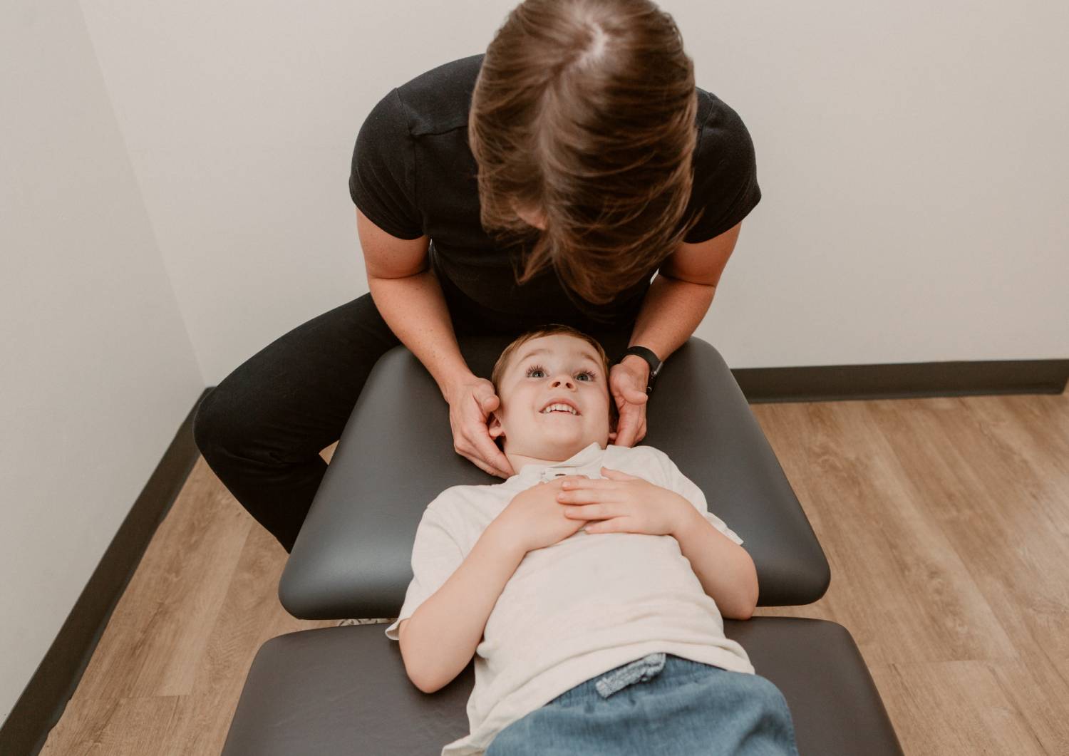 Practitioner performing a gentle neck assessment on a child lying on a treatment table in a clinic setting.