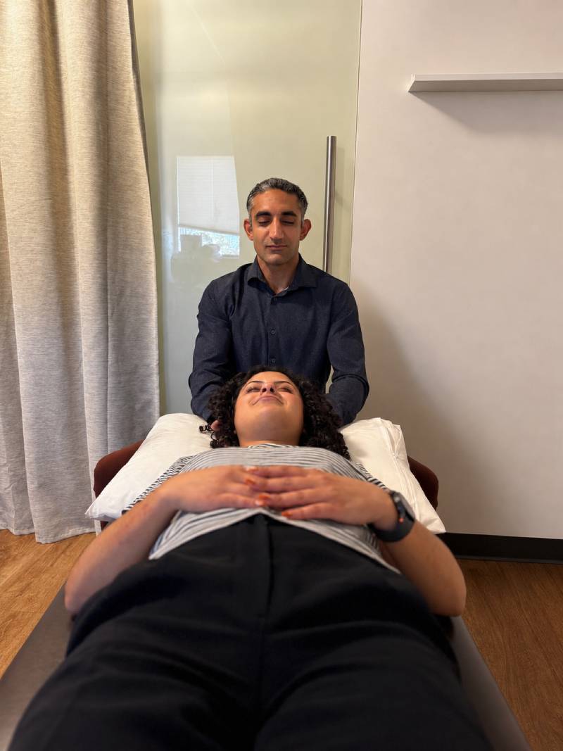 Person receiving a hands-on therapy treatment while lying on a treatment table in a modern wellness clinic, with the practitioner positioned at the head of the table.
