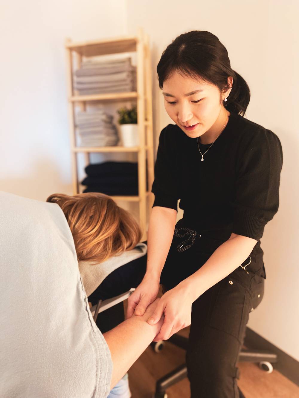 Massage therapist providing arm treatment to a client lying on a treatment table.